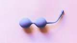 A purple kegel exercise device on a light pink background.