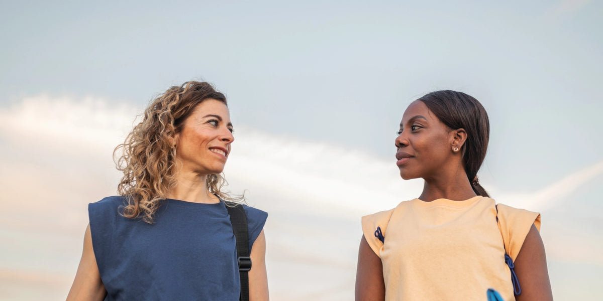 Two women are seen talking and smiling at the sky, reflecting a joyful and uplifting moment of friendship and connection.