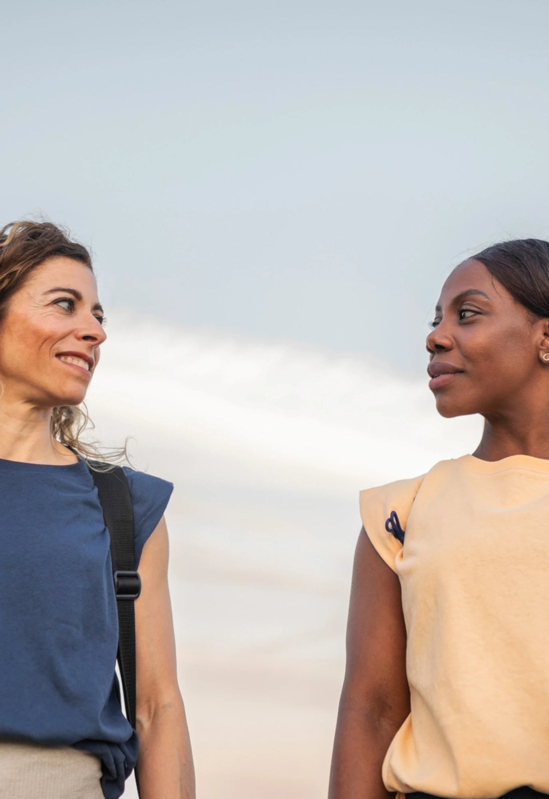 Two women are seen talking and smiling at the sky, reflecting a joyful and uplifting moment of friendship and connection.