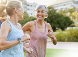 Two active women smiling and jogging together outdoors on a sunny day.