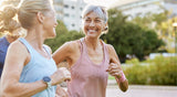 Two active women smiling and jogging together outdoors on a sunny day.